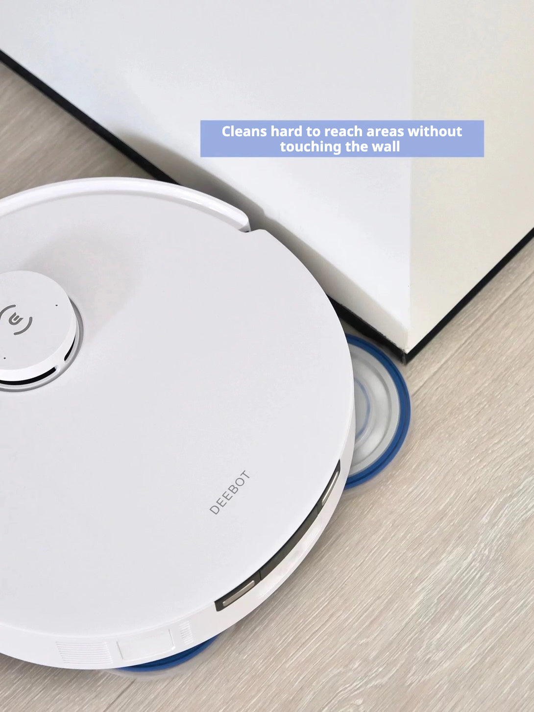 A white Ecovacs Deebot T30 Pro Omni robot vacuum cleaner cleaning near a wall without touching it. The text overlay reads, 'Cleans hard to reach areas without touching the wall