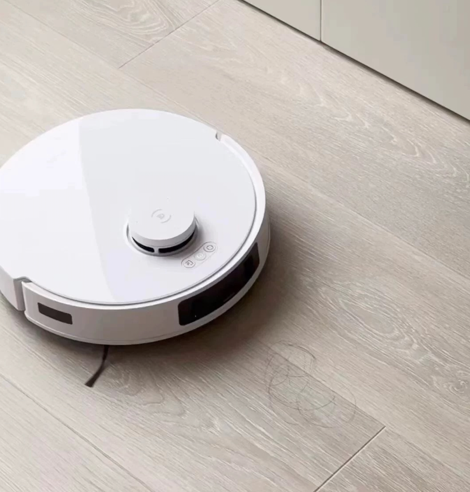 A white Ecovacs T30 Pro Omni robot vacuum cleaner in action on a light-colored hardwood floor, picking up dirt and debris